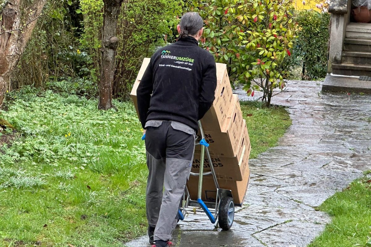 Ein Mitarbeiter von Tanner Umzüge fährt beschriftete Umzugskartons auf der Sackkarre über einen Gartenweg